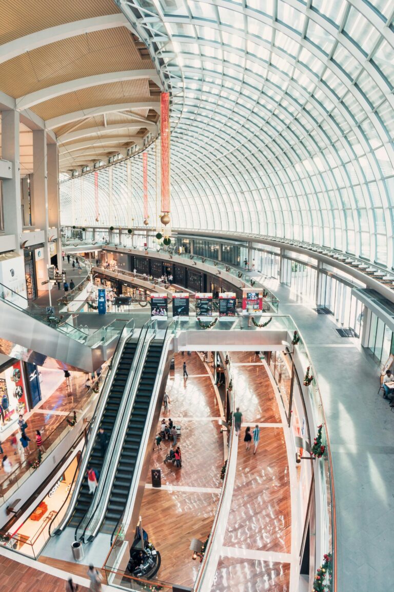 Spacious indoor shopping mall with glass ceilings and a modern design, including escalators and shops.